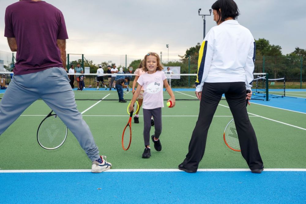 Child and adults playing a game on a tennis court