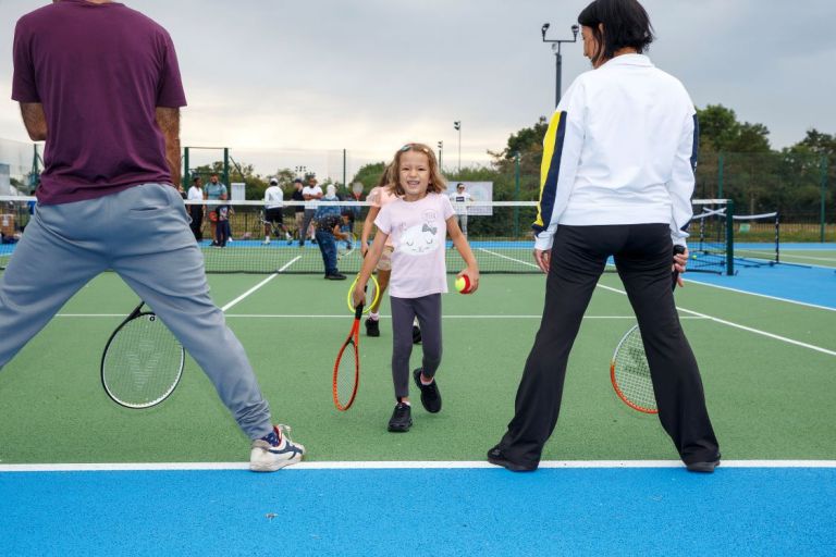 Child and adults playing a game on a tennis court